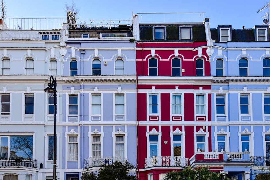 A row of ornate Victorian-style terraced houses in Notting Hill, featuring pastel blue and bold red facades with decorative white trim around multiple sash windows. The buildings are four stories high